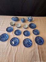 Full view of 19-piece child's Blue Willow tea set arranged on table, showing covered teapot, sugar, soup tureen, cups, plates, and saucers.
