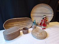 Photo of all five baskets, the clay head sculpture, and the antique Madame Hendren Native American character doll arranged on a white cloth with black background.