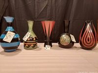 Front view of five handmade signed Peruvian pottery vases, showing their shapes and color patterns with tags visible on some.