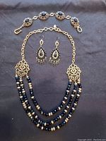 Photo showing the Lucky Brand 3-piece jewelry set: multi-strand faceted black bead necklace, coordinating faceted bead bracelet with gold-tone settings, and matching dangling earrings with iridescent beads.