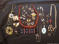 Full overview of the jewelry lot showing 12 pairs of earrings, 4 necklaces, amber strand, sterling silver rosary parts, Lucky Brand ring, brass buckle, Guatemalan beaded bracelet, and vintage brooches.