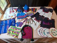 Overall view of entire collection on table showing embroidered blouses, scarves, bags, tortilla warmers, hats, bracelets, and bookmarks in various vibrant colors.