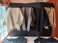 Front view of six woolen sweaters hanging on hangers showing color variations including off-white, brown, dark brown, black, and an embroidered off-white sweater.