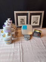 Full lot arrangement showing jars of Retinol and Hyaluronic acid facial creams, framed floral art pieces, Simplehuman shower mirror, and package of hearing aid batteries.