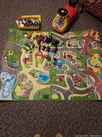 Overview of the toy collection showing City Town floor mat with various vehicles, box of LEGO bricks, and Mickey Mouse ride-on toy.