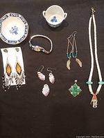Photo shows a collection of Native American jewelry, including various earrings, pendants, necklace, a watch band, and antique porcelain blue and white salt containers and small dish.