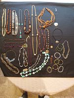 Full overview of all vintage necklaces and jewelry laid out on black fabric, showing bead styles, chains, pendants, and mixed materials.
