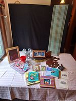 Full overview of all items on table including Polly Pocket toys, framed art, antique printed programs, books, wooden tramp art shelf, and small antiques