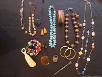 Full view of the lot laid on a black background showing over 15 pieces including necklaces, bracelets, bangles, earrings, a vintage brass padlock and key, Bakelite pieces, and assorted bead jewelry.