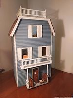 Front view of vintage blue wooden dollhouse with white shutters, porch, and rooftop railing.