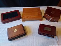 Five wooden hinged presentation boxes arranged on white surface, varying wood colors and styles visible.