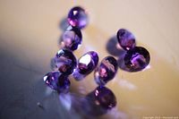 Close-up macro shot of 10 loose round cut purple amethyst gemstones showing facets and brilliance.