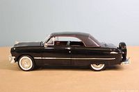 Side profile of the black 1950 Ford Convertible diecast model showing chrome details, whitewall tires and red interior visible through windows.