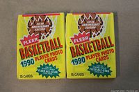 Front view of two unopened 1990 Fleer Basketball wax packs showing the yellow packaging with basketball and net graphic, stating Fifth Anniversary Edition and 15 cards per pack.