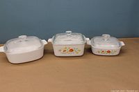 Photo of three Corning Ware casseroles with lids; two have orange and yellow floral designs.
