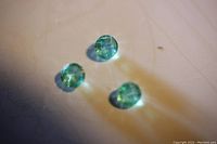 Photo of three light green round cut loose emeralds on a light surface showing color and size