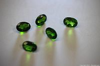 Five green oval cut diopside gemstones arranged on a white surface, showing their deep green color and faceted cuts.