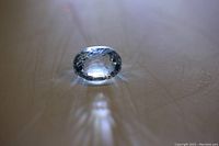 Close-up image of an oval cut light blue aquamarine gemstone showing facets and clarity on a plain surface.