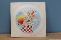 Front cover of a vinyl LP with cartoonish character with rainbow-colored hair, holding a peace sign, wearing a checkerboard shirt.