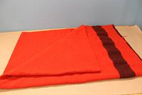 Red wool blanket folded showing a vibrant red color with a dark stripe near the edge.
