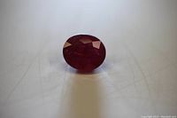 Oval cut deep red ruby gemstone on a plain surface.