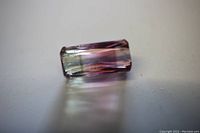 Close-up of rectangular cut watermelon tourmaline gemstone showing green to pink gradient colors and polished facets.