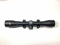 Side view of black Excalibur branded 32mm hunting scope with two attached mounting rings, showing adjustment knob in center.
