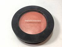 Front of bareMinerals Bounce & Blur blush showing coral powder product behind clear lid with bareMinerals branding.