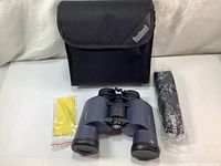 Binoculars, black carrying case, cleaning cloth and lens covers laid on white surface