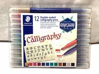 Front view of Staedtler 12-pack double-ended calligraphy pens in sealed plastic packaging with label and pen colors visible.