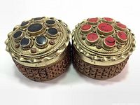 Pair of vintage brass trinket boxes showing decorated lids with black and red stones and carved sides.