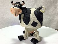 Front view of black and white ceramic cow figurine with bobbing head, showing textured body and facial details.