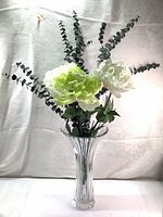 Clear glass vase with tall vertical ridges holding three artificial flowers and eucalyptus sprigs, showing full front view