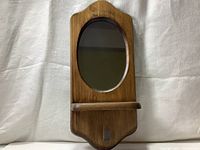 Front view of vintage wooden wall shelf showing oval mirror and small shelf ledge below.