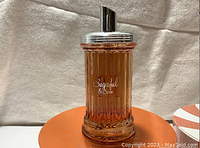 Close-up photo of the glass perfume bottle showing amber liquid inside with silver atomizer top.