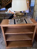 Front view of smaller Aspen Furniture bookcase with three shelves, small brass lamp on mini woven runner on top
