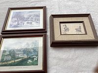 Three framed prints hanging on white textured wall, including one smaller sketch framed with fabric mat and two larger prints with wood brown frames.