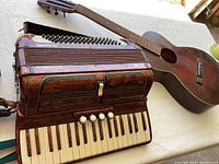 Photo showing the Baldoni accordion alongside the old guitar, highlighting the burl finish and keyboard keys on the accordion.