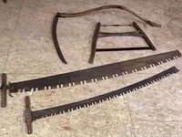 Photo showing the full set of antique logging and woodworking tools arranged on a wood floor with detailed view of the blades and frames.