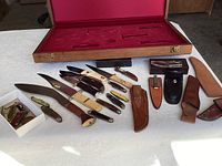 Overview of knives and sheaths laid out before red velvet-lined presentation box lid