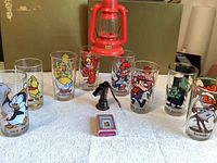 Photo showing 8 clear vintage cartoon character glasses and a small red toy lantern, miniature cards. Characters include Woody Woodpecker, Bullwinkle, Winnie the Pooh, Big Baby Huey, and others.