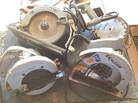 Three corded circular saws visible, two Skil saws and one Rockwell, along with several extra saw blades on a surface.