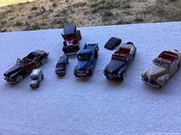 Top view showing seven classic car model replicas on a white tablecloth with outdoor background.