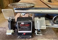Close-up of the Craftsman bench grinder positioned in front of the table saw showing protective shields and power switch with label.