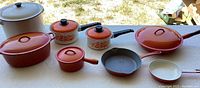 All cookware items arranged outside on a table showing the orange Descoware and white unmarked pieces.