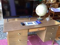 Wooden desk displaying Vizio monitor, globe, lamp, and some items on top of desk.