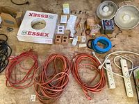 Photo showing assorted electrical supplies including orange extension cords, white faceplates, switches, outlets, and the Essex brand box of electrical wire.