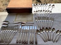 Full view of entire flatware set including forks, knives, spoons, salad servers, butter knife, sugar spoon, wooden boxes, and authenticity certificate laid out on table.