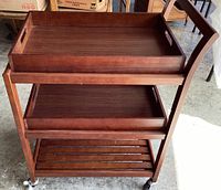 Wooden rolling cart visible from the front showing two removable trays and slatted lower shelf.