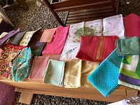 Overview of assorted scarves spread on wooden surface with various colors and patterns including floral, stripes, and geometric designs.